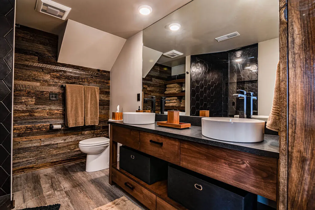 A contemporary bathroom featuring dual vessel sinks on a wooden vanity and a stylish hexagon tile shower. The lighting is serene, and the space feels spa-like, ideal for refreshing morning or night routines.