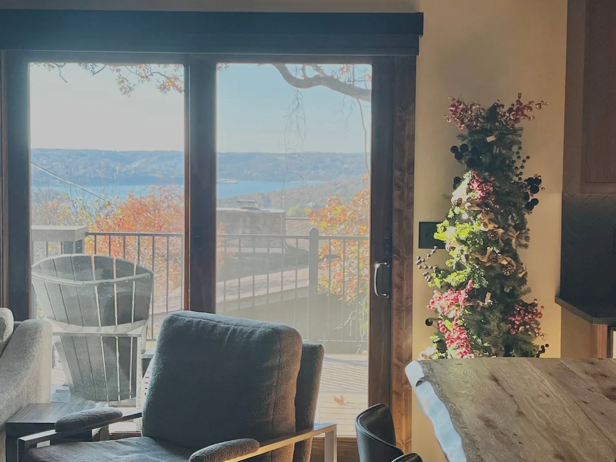 A serene seating area with modern, comfortable chairs, large windows framing the lake and treetops, and a decorative plant. The light and airy design encourages both relaxation and social interaction while offering a direct connection to the outdoors.