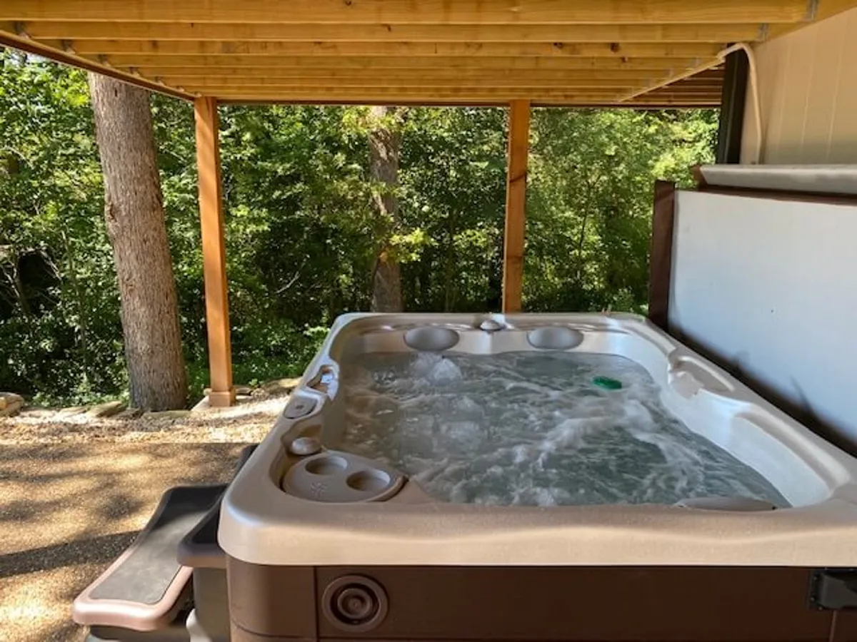 This image centers on a hot tub set on a deck, surrounded by trees and wooden railings, with a tranquil, private atmosphere perfect for relaxation. The setting hints at stargazing opportunities and the soothing presence of nature, closely aligning with the section's highlight of a private hot tub experience on the lower deck.