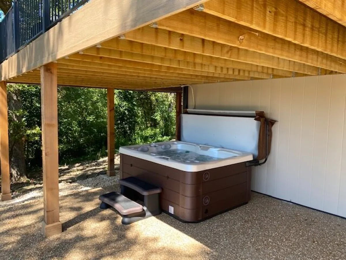 This image features a tranquil wooden deck nestled amid lush greenery, with a private hot tub invitingly placed to one side. The natural setting and outdoor amenities evoke a sense of luxurious relaxation, perfect for unwinding with friends or alone while immersed in nature.