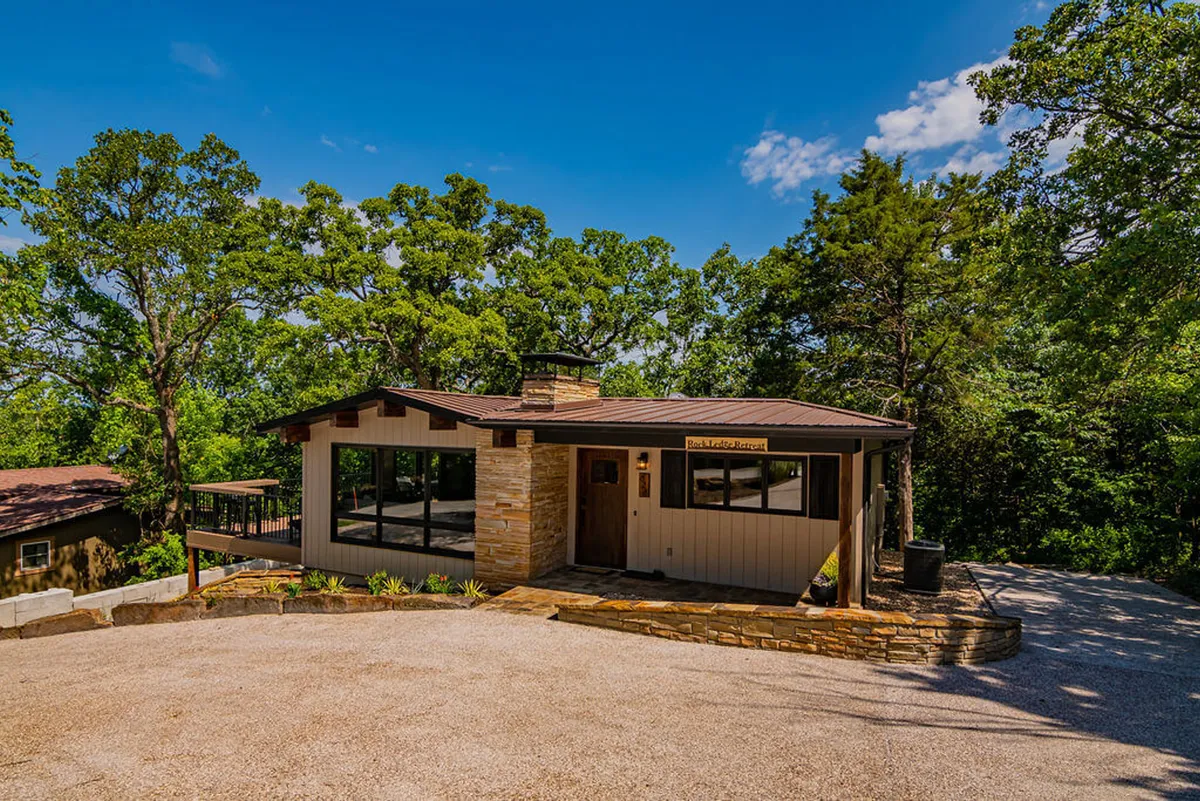 This exterior view highlights the home's stone facade, large windows, and a landscaped pathway leading to the entrance, all set amidst verdant surroundings. The architecture blends with the landscape, evoking a sense of arrival and anticipation for exploration.
